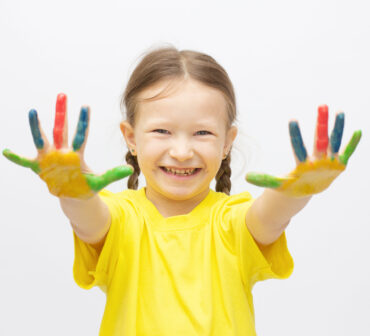 Happy cute little girl with colorful painted hands isolated on a white education concept